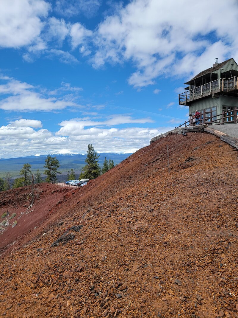 Picture of the fire tower on top of a mound of rust red cinders, with a blue sky in the background